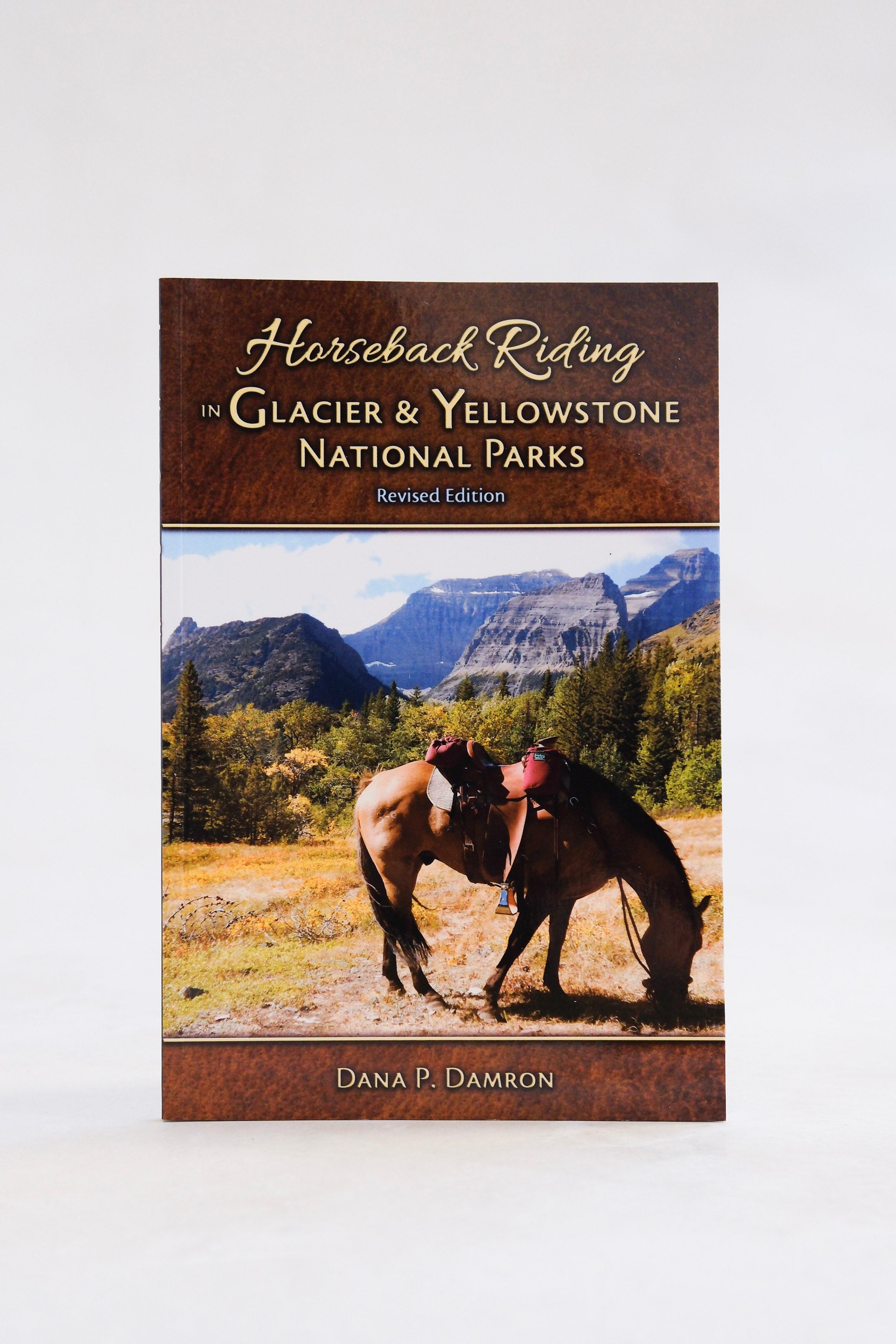 Cover of the Farcountry Press book, "Horseback Riding in Glacier & Yellowstone National Parks," depicting a photo of two horses grazing along scenic trails amid a breathtaking mountainous landscape.